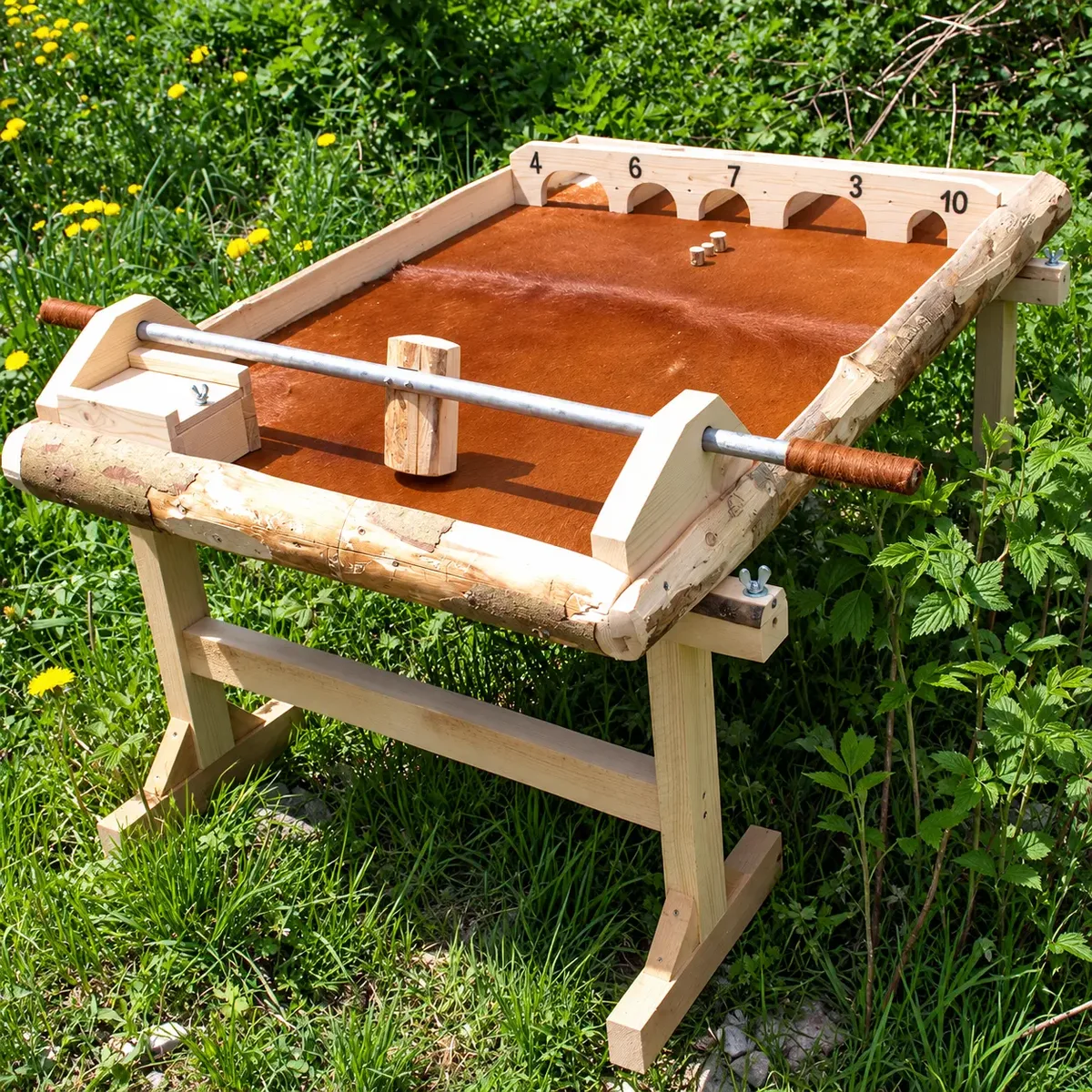 Holzklotzkicker: rustikales Holzspiel mit brauner Fellbespannung, Spielstab mit Holzhammer und Zielbögen mit Punktezahlen, im Freien auf einer Wiese – Holzspiel zum Mieten im Hochschwarzwald
