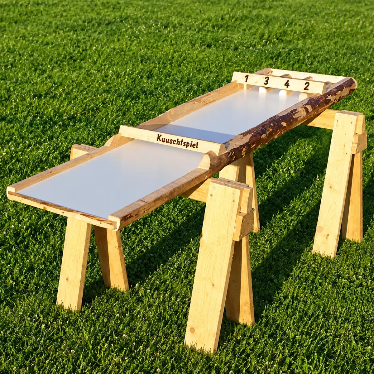 Kuuschtspiel: lange, helle Spielfläche mit Seitenbanden aus gespaltenen Baumstämmen, mittigem Torbalken und Zielfächern auf drei Holzböcken – Holzspiel zum Mieten im Hochschwarzwald