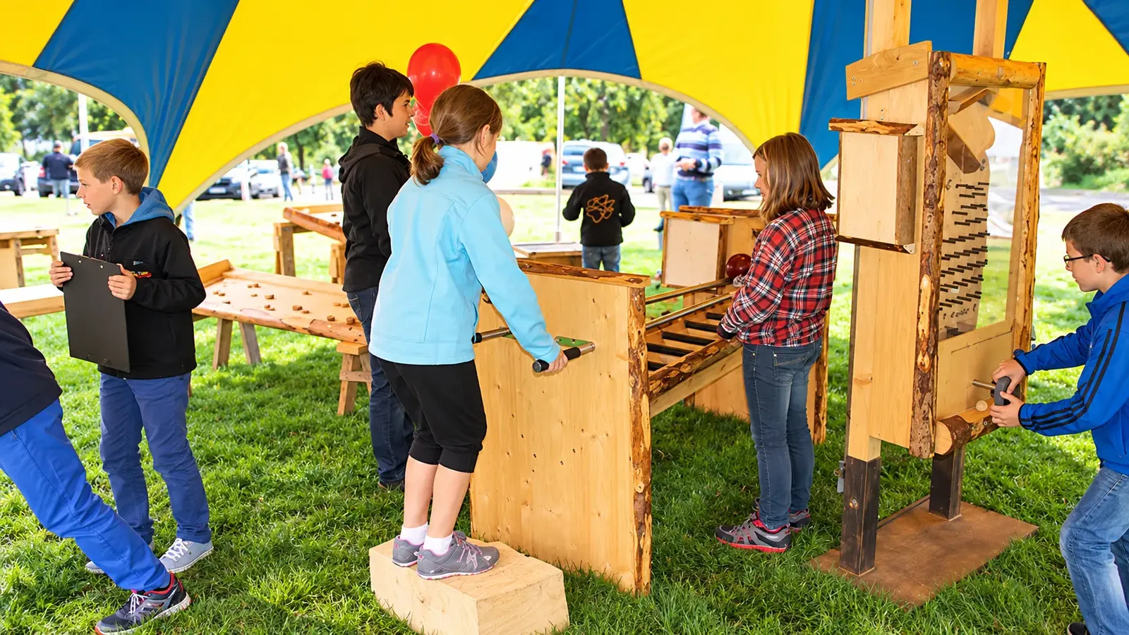 Kinder spielen unter einem bunten Festzelt an Holzbahnen und einem Kugelspiel