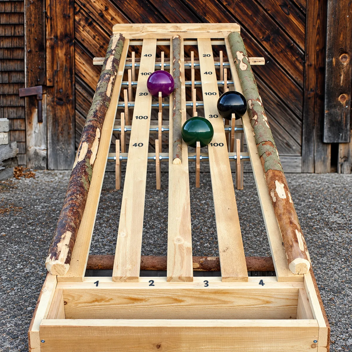 Punkte Roller: lange Holzspielbahn mit Rindenkanten, Klappstäben, Punktezahlen und farbigen Bowlingkugeln vor einem Scheunentor – Holzspiel zum Mieten im Hochschwarzwald